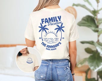 May include: A white t-shirt with a blue graphic design on the back. The graphic features palm trees, a sunset, and the text "FAMILY Vacation THE JOHNSON'S MAUI, HAWAII". The shirt also has the text "CHARLOTTE" on the front.