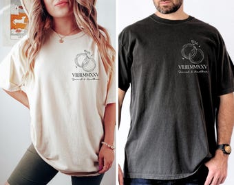 May include: Two t-shirts with a graphic of two intertwined rings with stars above them. The text below the rings reads "VIII.III.MMXXV Daniel & Heather". One shirt is a light beige color and the other is a dark charcoal color.