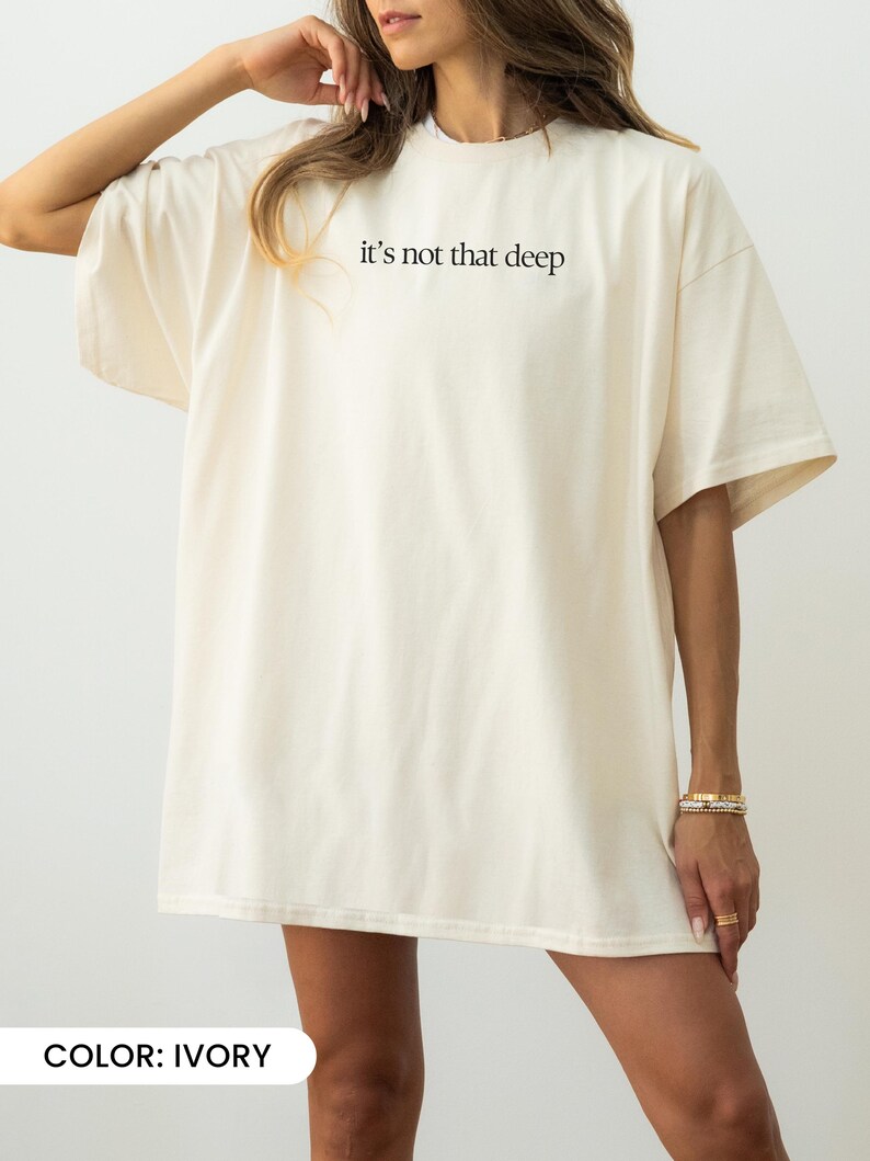 May include: An oversized white t-shirt with the text "it's not that deep" printed on the front. The shirt is made from a soft, comfortable fabric and has a relaxed fit.