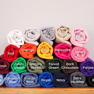 May include: A variety of rolled up t-shirts in different colors, including maroon, light blue, carolina blue, indigo blue, royal blue, navy, dark heather, black, purple, safety pink, heliconia, gold, orange, red, white, ash, sport grey, and light pink.