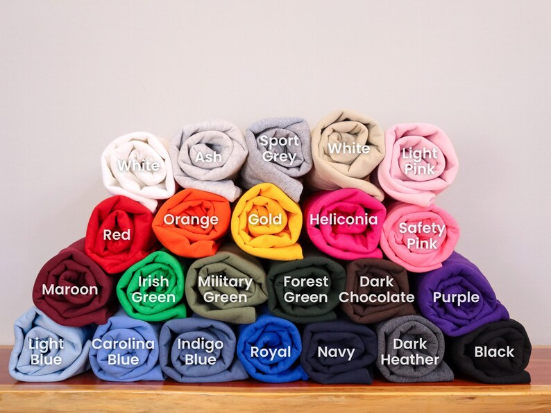 May include: A variety of rolled up t-shirts in different colors, including maroon, light blue, carolina blue, indigo blue, royal blue, navy, dark heather, black, purple, safety pink, heliconia, gold, orange, red, white, ash, sport grey, and light pink.