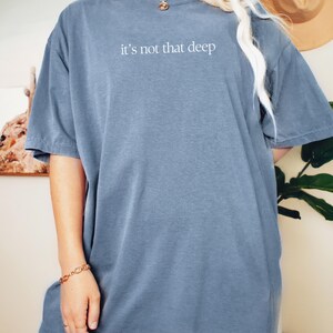 May include: An oversized t-shirt in blue jean colour with the text "it's not that deep" in white.