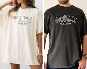 May include: Two oversized t-shirts, one white and one black, with the words "BRIDE" and "GROOM" in a collegiate font. The date "VIII.III.MMXV" is printed below each word.