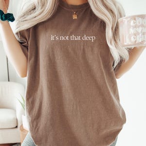 May include: An oversized brown t-shirt with the text "it's not that deep" printed in white. The shirt is made from a soft, comfortable material and has a relaxed fit.