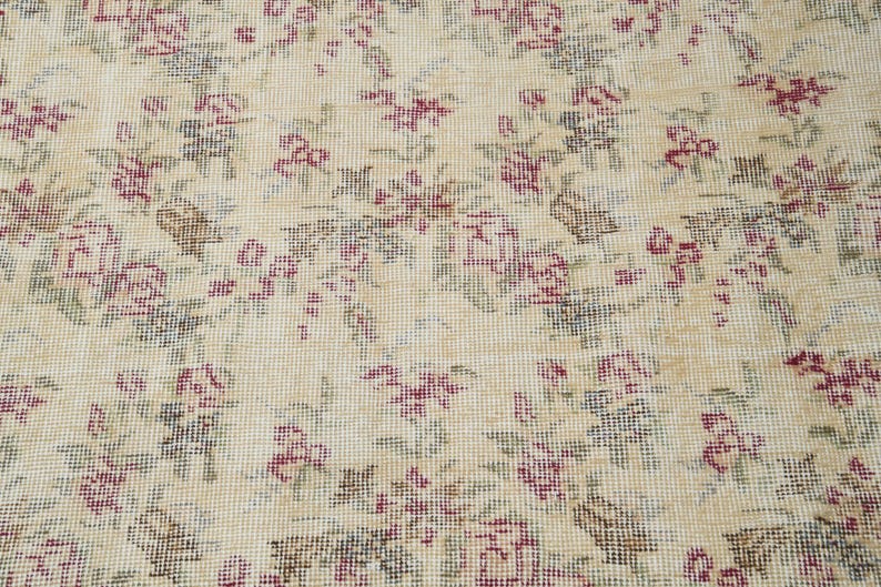 May include: A beige rug with a floral pattern in shades of pink and green. The rug has a woven texture and a delicate design.