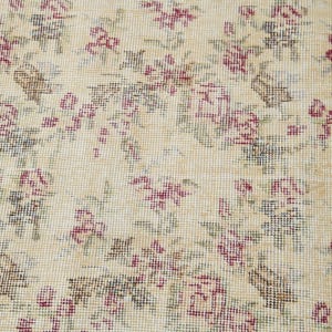 May include: A close-up of a beige rug with a floral pattern. The rug is woven with small, intricate details and features a repeating design of pink and green flowers.