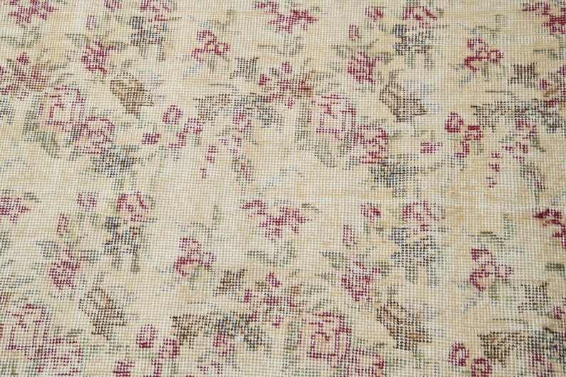 May include: A close-up of a beige rug with a floral pattern. The rug is woven with small, intricate details and features a repeating design of pink and green flowers.