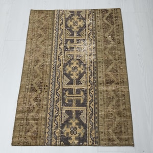 May include: A vintage runner rug with a brown and beige color scheme. The rug has a central stripe with a geometric pattern in shades of brown, beige, and white.
