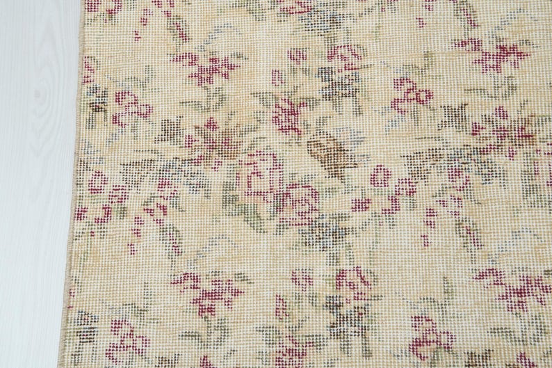 May include: A beige rug with a floral pattern. The flowers are pink and green and are woven into the rug.