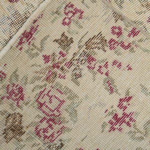 May include: Close-up of a beige rug with a floral pattern. The rug has a woven texture and features small red, brown, and green flowers.