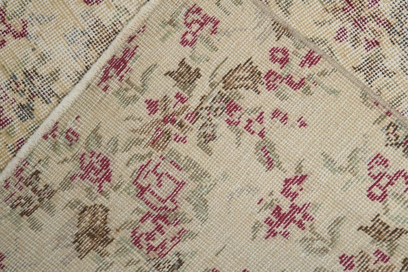 May include: Close-up of a beige rug with a floral pattern. The rug has a woven texture and features small red, brown, and green flowers.