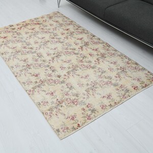 May include: A vintage floral patterned rug with a cream background and pink and red floral accents. The rug is laid out on a white wood floor.