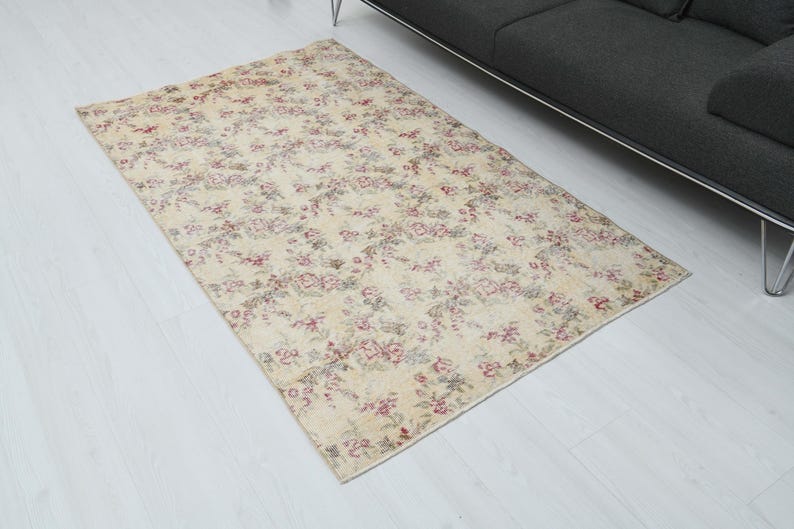 May include: A vintage floral patterned rug with a cream background and pink and red floral accents. The rug is laid out on a white wood floor.