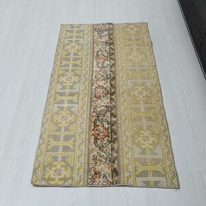May include: A light beige and yellow runner rug with a floral pattern. The rug has a geometric design with a central floral motif.