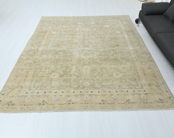 Könnte beinhalten: Ein großer, rechteckiger, beigefarbener Teppich mit einem komplizierten, verblassten Blumenmuster. Der Teppich hat einen detaillierten Rand mit kleinen, dunkelblauen Akzenten. Der Teppich liegt auf einem weißen Boden, im Hintergrund ist ein dunkelgraues Sofa zu sehen.