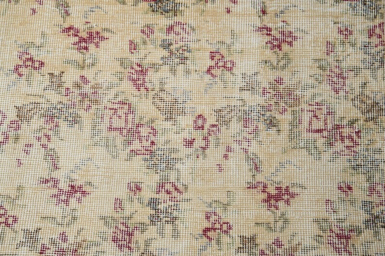 May include: Close-up of a beige fabric with a floral pattern. The fabric is woven with small, intricate details, creating a delicate and vintage aesthetic. The flowers are a pale pink color and are scattered throughout the fabric.