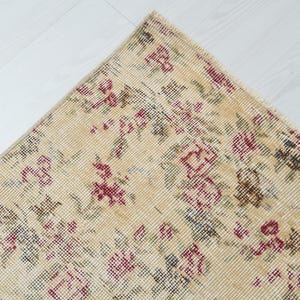 May include: A beige rug with a floral pattern in shades of pink, green, and blue. The rug has a distressed look, giving it a vintage feel.