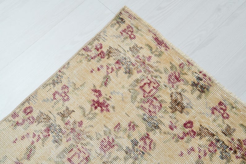 May include: A beige rug with a floral pattern in shades of pink, green, and blue. The rug has a distressed look, giving it a vintage feel.