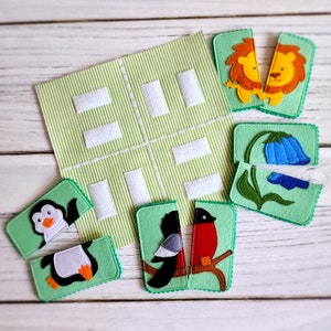 May include: A green felt board with white squares and a variety of felt animal and flower puzzle pieces. The pieces include a penguin, a bird, a lion, and a flower.