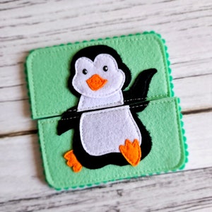 May include: A felt penguin puzzle with two pieces. The penguin is black and white with an orange beak and feet. The puzzle pieces are on a green felt background.
