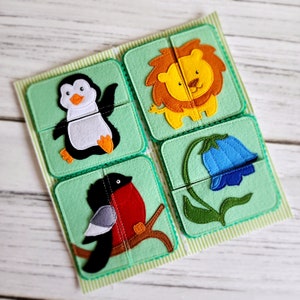 May include: A felt puzzle with four pieces featuring a penguin, a lion, a flower, and a bird. The puzzle pieces are on a green background with white stitching.