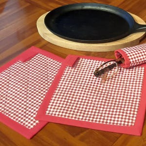 May include: Two red and white gingham fabric hot pads with red trim. A red and white gingham fabric glasses case with glasses inside is on top of the hot pads.