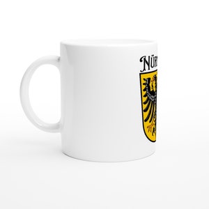 Puede incluir: Taza de cerámica blanca con un escudo de armas negro y amarillo con un águila y el texto "Nürnberg" en negro.