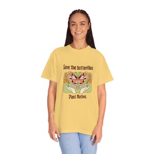 Könnte beinhalten: Ein gelbes T-Shirt mit einem Aufdruck eines Schmetterlings in einer Hand. Der Text "Save the butterflies Plant Native." ist auf dem T-Shirt gedruckt.