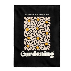 Peut inclure: Jeté de canapé noir avec du texte blanc qui dit "Would Rather Be Gardening" et un motif de marguerites blanches avec des centres jaunes.