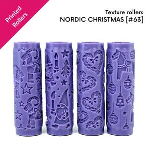 以下が含まれることがあります： Printed Rollers NORDIC CHRISTMAS [#63]とラベルされた4本の紫色の円筒形テクスチャーローラー。各ローラーには、ノーム、星、ハート、馬、鐘、クリスマスツリーなどのエンボス加工された模様が施されており、柔らかい素材に型押しをするために使用されます。