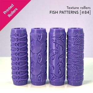 Puede incluir: Cuatro rodillos de textura cilíndricos de color morado con patrones de peces en relieve, etiquetados como Printed Rollers y FISH PATTERNS [#84]. Cada rodillo muestra un diseño acuático distinto, incluyendo peces pequeños y carpas koi.