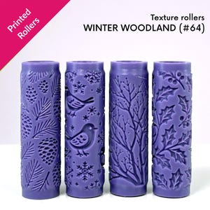 Puede incluir: Cuatro rodillos de textura morados con diseños de bosque invernal. Los rodillos presentan patrones de piñas, pájaros, ramas y hojas de acebo. El texto "Printed Rollers" y "WINTER WOODLAND (#64)" son visibles.