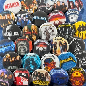 K&ouml;nnte beinhalten: Eine Sammlung runder Metall-Ansteckbuttons mit der Band Metallica. Die Buttons zeigen verschiedene Bilder, darunter Bandmitglieder, Albumcover und das Logo der Band. Die Buttons sind in verschiedenen Farben erh&auml;ltlich, darunter Schwarz, Wei&szlig;, Rot und Blau.