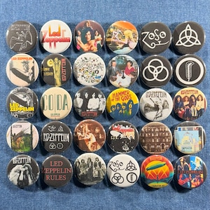 May include: A collection of 30 round Led Zeppelin button pins. The pins feature various album art, band logos, and text, including "Led Zeppelin," "CODA," and "Hammer of the Gods." The pins are in various colors, including black, white, yellow, and red.