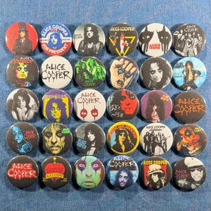 May include: A collection of 30 round Alice Cooper buttons. The buttons feature images of Alice Cooper, album art, and text such as "Alice Cooper for President" and "School's Out". The buttons are in various colors, including red, black, white, and blue.