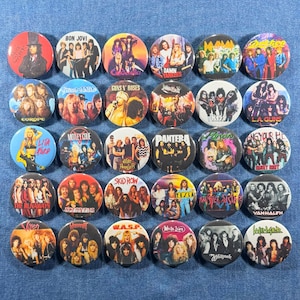 May include: A collection of round pinback buttons featuring various rock bands. Bands include Bon Jovi, Guns N' Roses, Motley Crue, and others. Each button has a colorful design with band names and images.