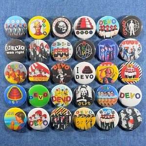 May include: A collection of thirty-two round Devo band buttons with various designs. The buttons feature images of the band members, logos, and text such as "DEVO," "DEVO was right," and "Whip It." The buttons are in various colors, including red, yellow, and blue.