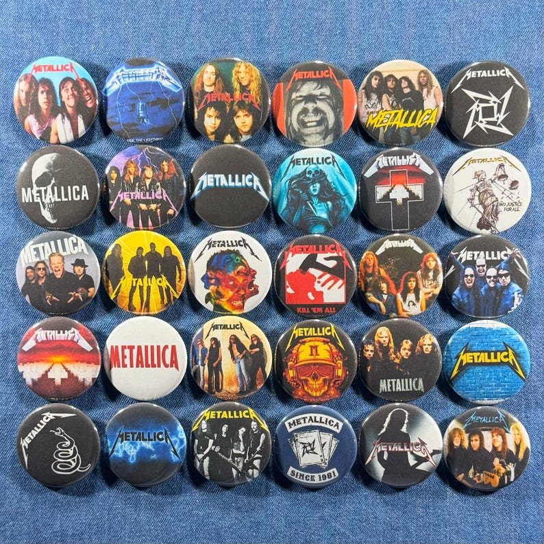 K&ouml;nnte beinhalten: Eine Sammlung runder Metallica-Bandbuttons mit verschiedenen Bildern und Logos. Die Buttons zeigen Bandmitglieder, Albumcover und das Metallica-Logo. Die Buttons befinden sich auf einem blauen Jeans-Hintergrund.