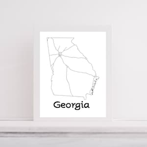 May include: A framed print featuring a minimalist line drawing of the state of Georgia in black against a white background. The word "Georgia" is printed in a bold, black font below the map.