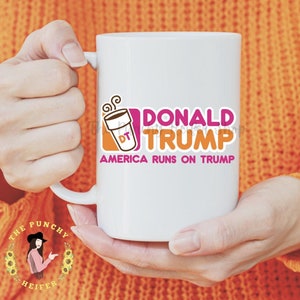 May include: White ceramic mug with a pink and orange graphic of a coffee cup with the text "DONALD TRUMP" and "AMERICA RUNS ON TRUMP".