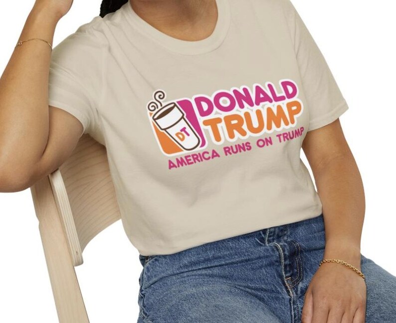 May include: A beige t-shirt with a pink and orange graphic of a coffee cup with the text "Donald Trump" and "America Runs on Trump".
