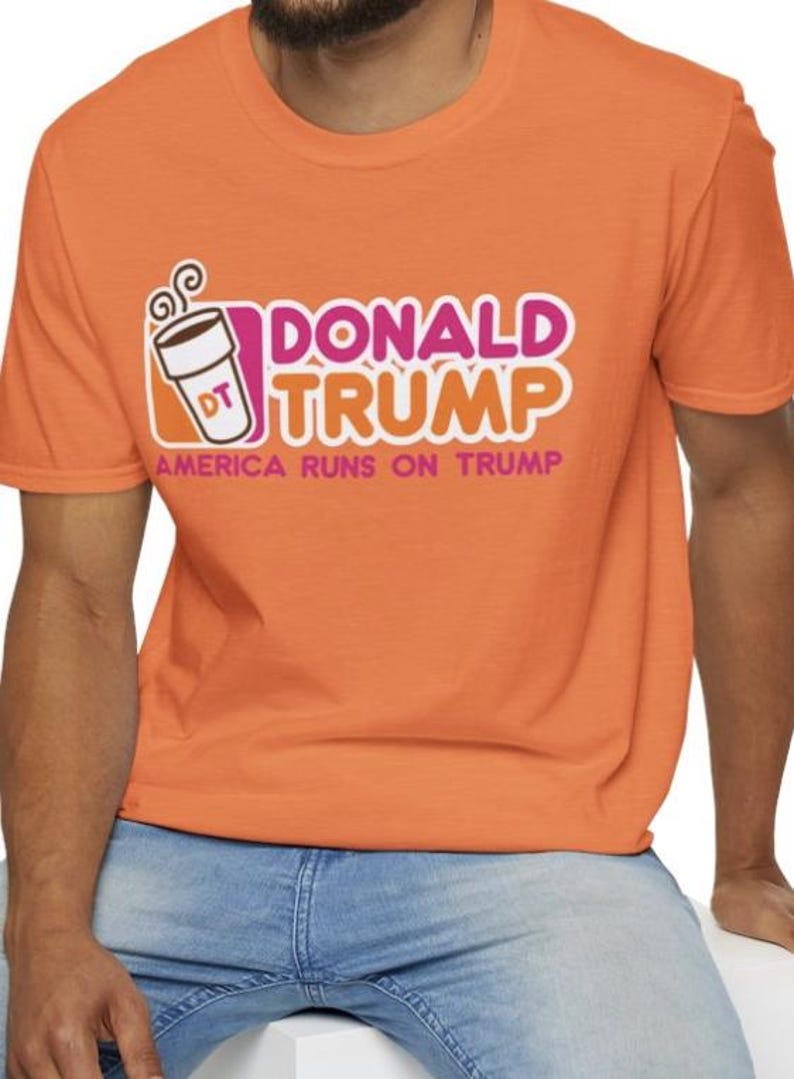 May include: Orange t-shirt with a pink and white graphic of a coffee cup with the text "Donald Trump" and "America Runs on Trump".