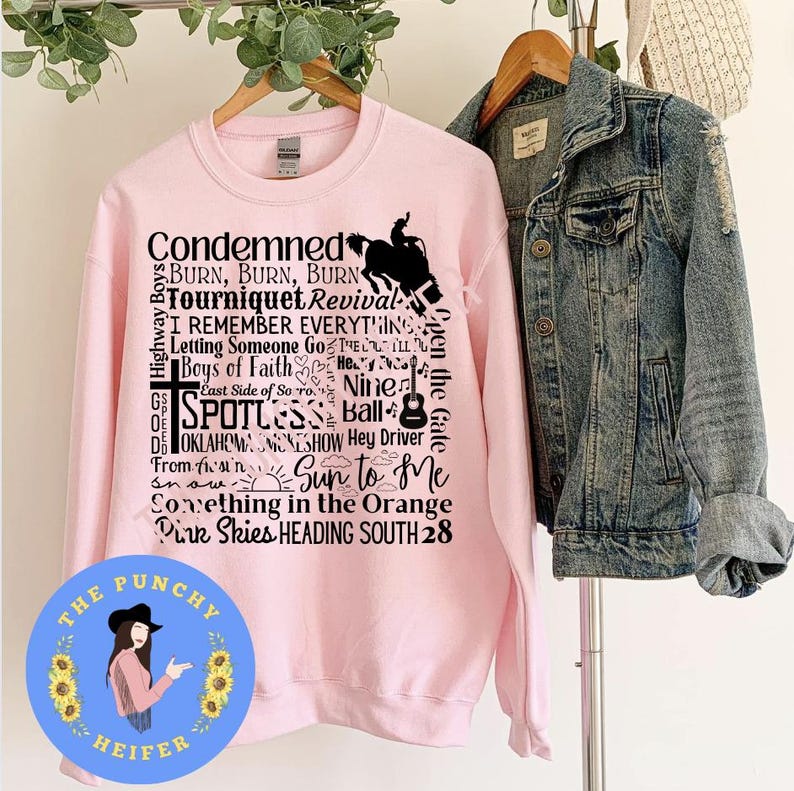 May include: Pink sweatshirt with black text that reads "Condemned", "Burn, Burn, Burn", "Tourniquet Revival", "I Remember Everything", "Letting Someone Go", "The Ill", "Boys of Faith", "He", "Nine", "East Side of So ro", "Spotless", "Ball", "DE OKLAHOMA", "MONESHOW", "Hey Driver", "From fin", "Sun to Me", "Something in the Orange", "Pink Skies HEADING SOUTH 28".