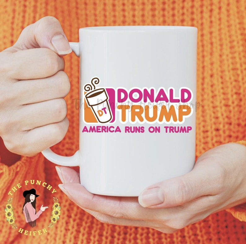 May include: White ceramic mug with a pink and orange graphic of a coffee cup with the text "DONALD TRUMP" and "AMERICA RUNS ON TRUMP".