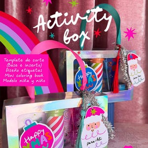Pode incluir: Uma caixa de atividades festiva com uma alça de arco-íris e as palavras "Activity box" em escrita branca. A caixa contém itens coloridos e é decorada com etiquetas e adesivos com tema de Natal. A caixa tem uma fita rosa e um design de arco-íris.