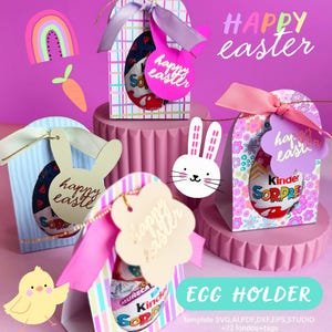 Puede incluir: Soportes para huevos de Pascua con diseños coloridos. Cada soporte contiene un huevo Kinder Sorpresa y está decorado con cintas y etiquetas que dicen "Happy Easter". La imagen también incluye un arcoíris, una zanahoria y un pollito.