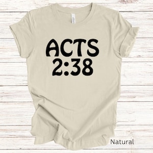 Op de afbeelding: Een beige T-shirt met zwarte tekst die "ACTS 2:38" zegt.