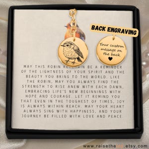 Könnte beinhalten: Ein goldfarbener Schlüsselanhänger mit einem runden Anhänger, der eine detaillierte Illustration eines Rotkehlchens zeigt. Die Rückseite des Anhängers ist mit dem Text "Ihre individuelle Botschaft auf der Rückseite" graviert. Der Schlüsselanhänger wird in einer kleinen Schachtel mit einer Botschaft über das Rotkehlchen als Erinnerung an die Leichtigkeit des eigenen Geistes geliefert.