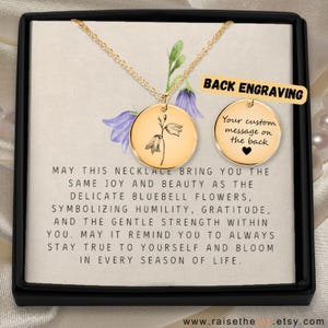 May include: A gold-toned circular pendant necklace featuring a delicate bluebell flower engraving on a chain. A second circular disc shows the text BACK ENGRAVING and Your custom message on the back with a heart icon. The card includes inspirational text.