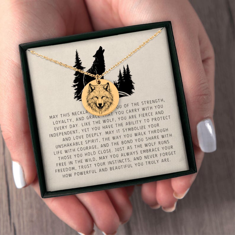 K&ouml;nnte beinhalten: Eine goldfarbene Halskette mit einem runden Anh&auml;nger mit Wolfsdesign. Der Anh&auml;nger h&auml;ngt an einer zarten Kette. Die Halskette wird in einer schwarzen Schachtel mit Text &uuml;ber St&auml;rke und Loyalit&auml;t pr&auml;sentiert.